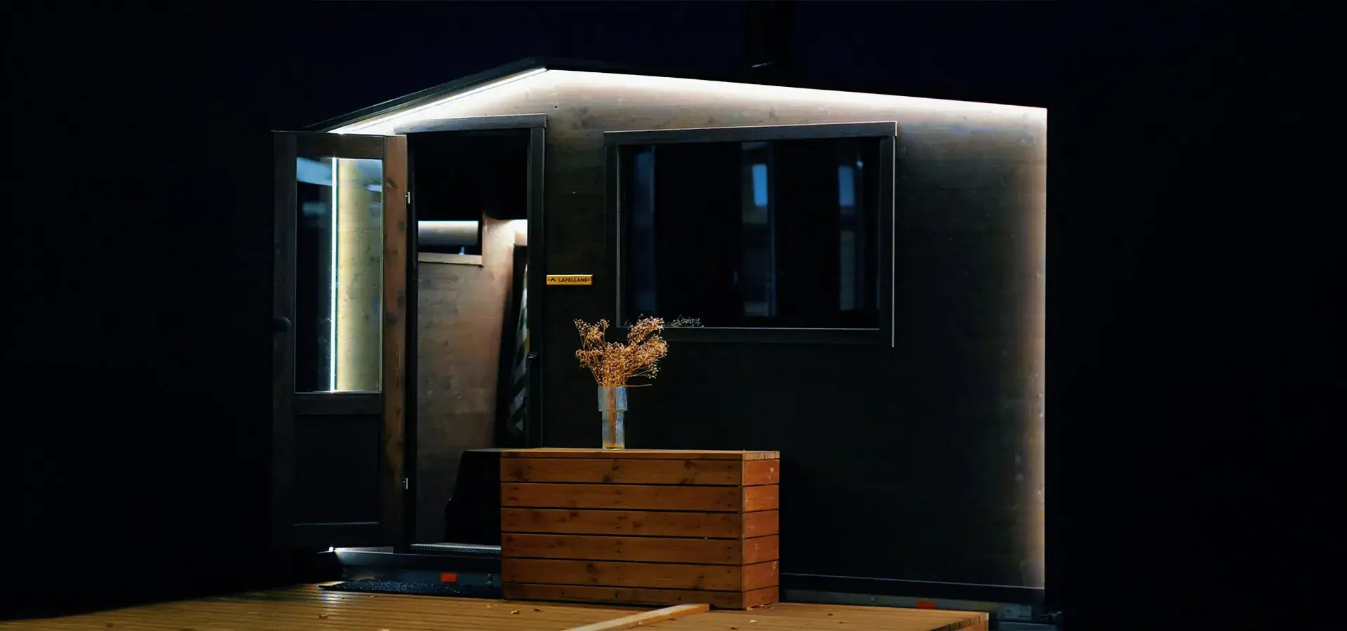 Tunnelmallisesti valaistu Lapelland Vaunusauna S iltahämärässä, jossa näkyvät erillinen pukuhuone ja suuri panoraamaikkuna.