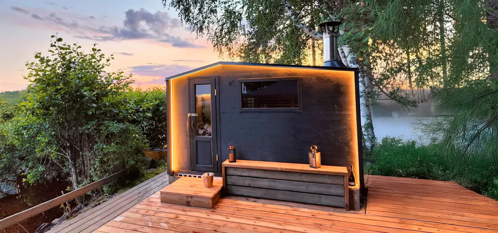 Moderni Lapelland Saunavaunu S sijoitettuna kotipihaan, varustettuna terassilla, LED-valaistuksella ja suurella maisemaikkunalla.